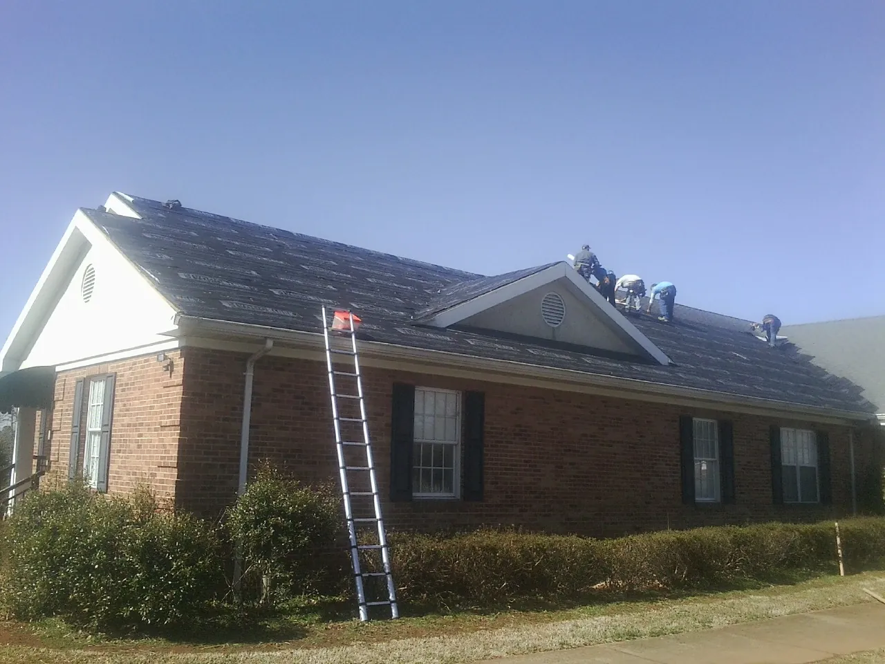 Crew tearing shingles off a brick ranch roof with a ladder set — Metal Roof Repair work by our crew in Mehama