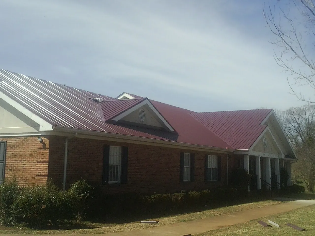 Red metal roof with gabled entries on a long brick building, from a Hail Damage Roof Repair job in Mehama