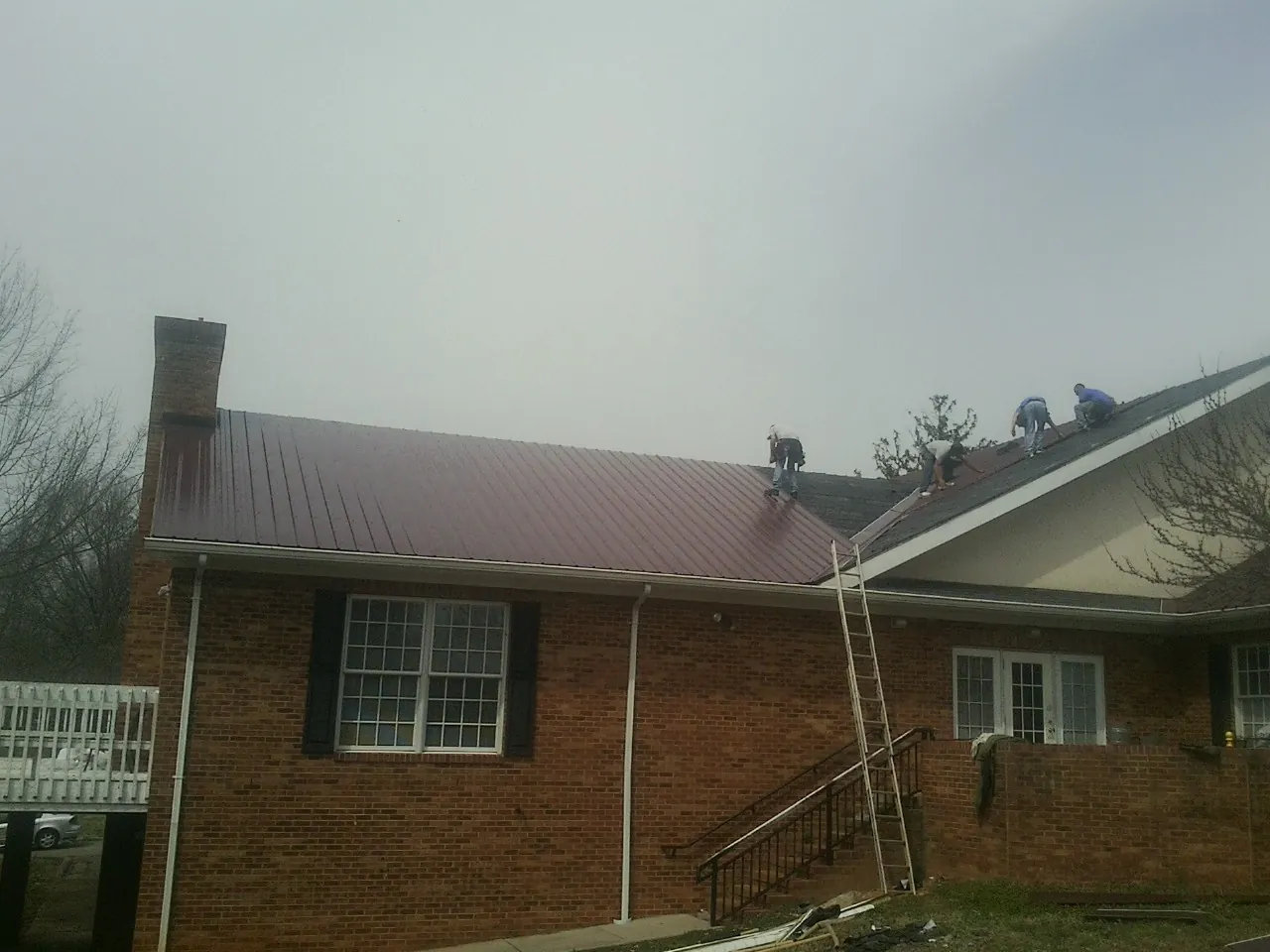 Crew setting red metal roofing panels on a brick home in Mehama