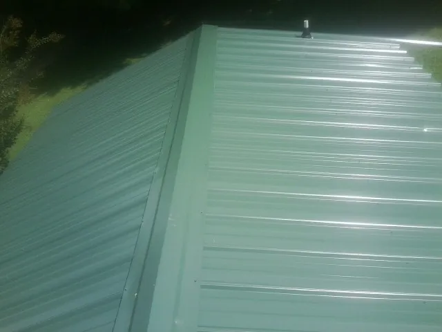 New green metal panels meeting at the ridge of a roof — Flat Roof Repair work by our crew in Mehama