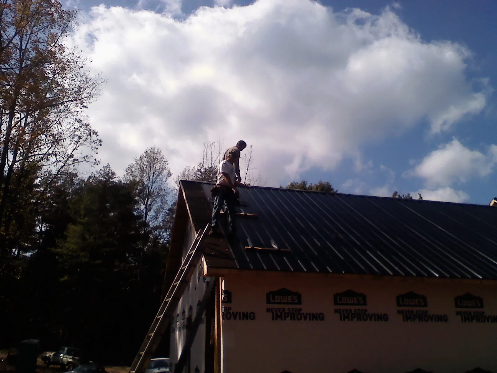 Roofer fastening dark metal panels high against a cloudy sky, from a Roof Inspection job in Mehama