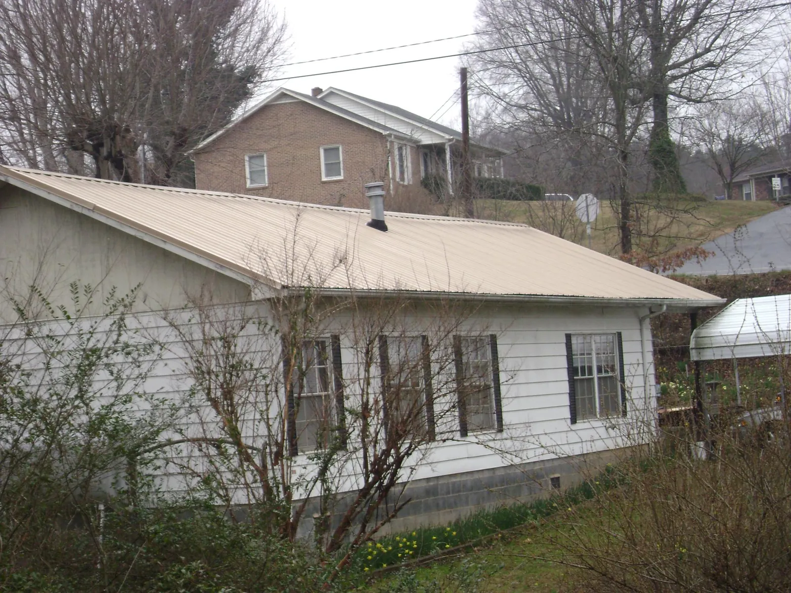 Tan metal roof on a white sided house set into a hillside — Commercial Roofing by Roofing Brothers in Mehama